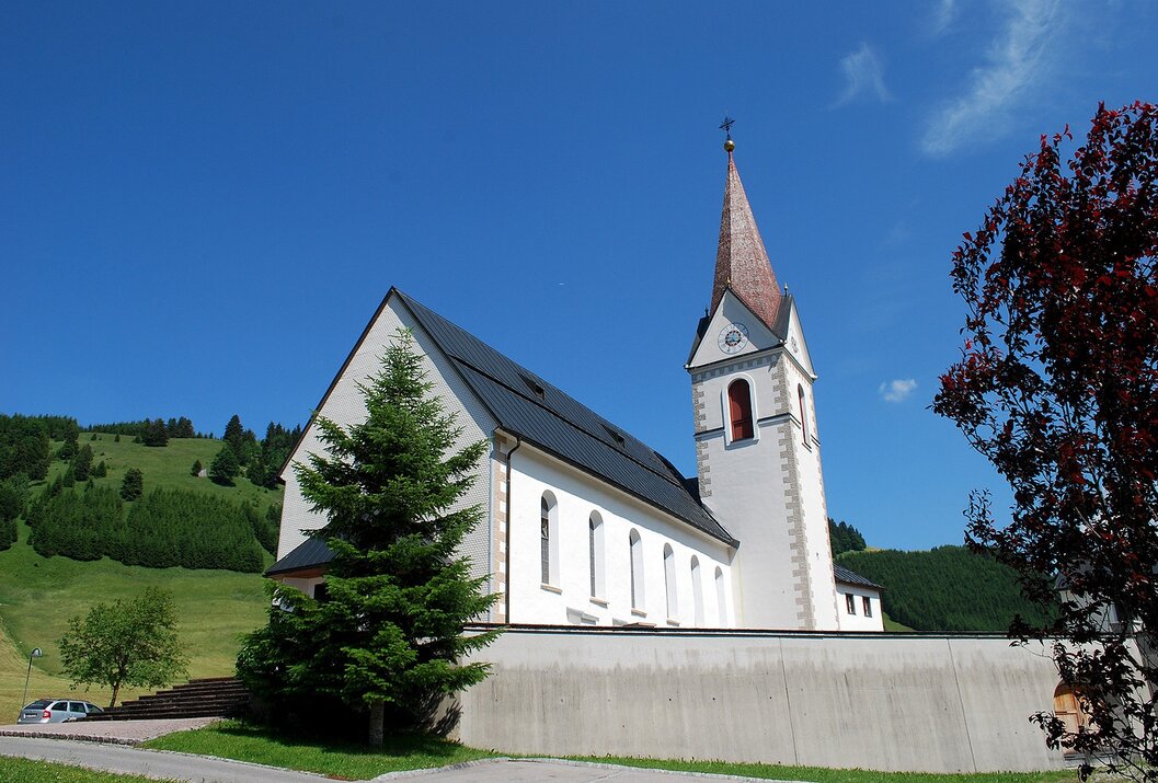 Weiße Kirche mit rotem Kirchturm vor blauem Himmel und grüner Hügellandschaft