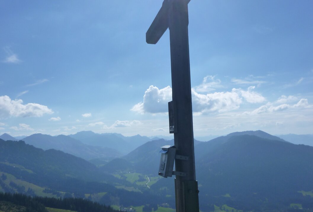 Gipfelkreuz vor Bergpanorama und blauem Himmel mit Sonne