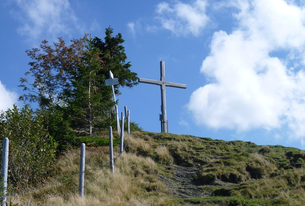 Gipfelkreuz auf Hügel unter blauem Himmel mit Wolken