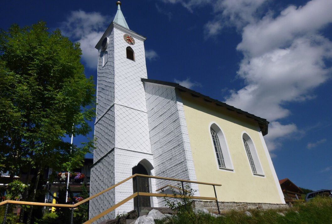 Kleine Kirche mit weißem Turm und gelber Fassade vor blauem Himmel