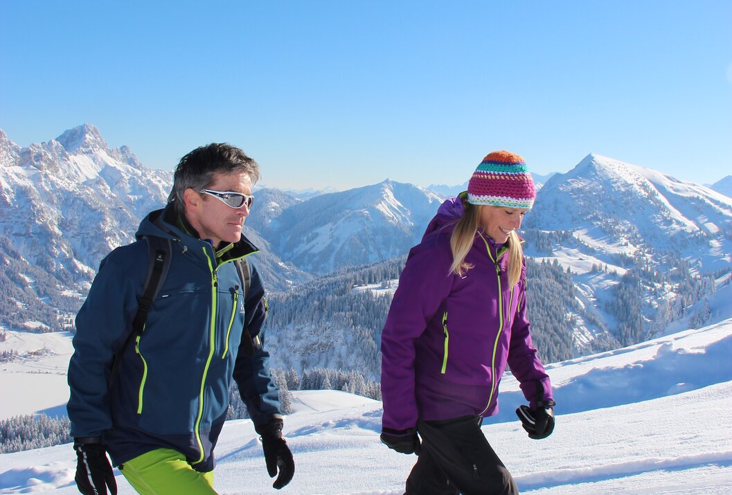 Zwei Personen wandern im Schnee vor Bergpanorama