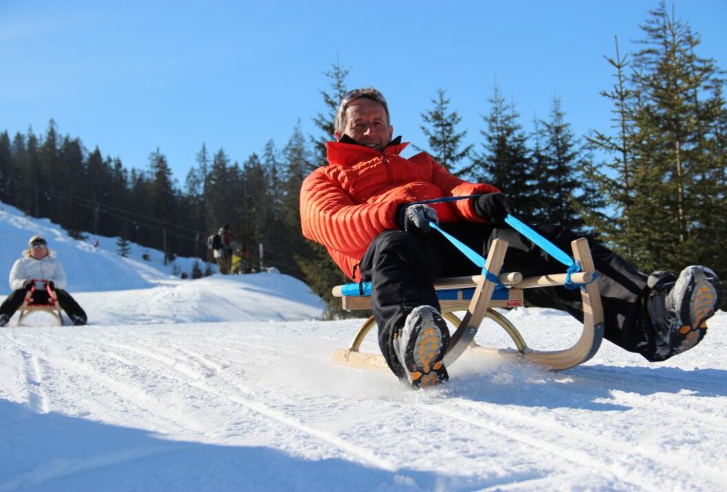Mann mit roter Jacke fährt Schlitten im Schnee