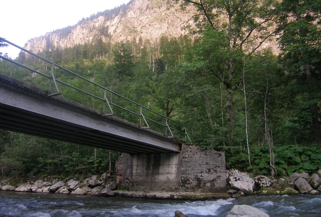 Brücke über Fluss vor bewaldetem Berghang