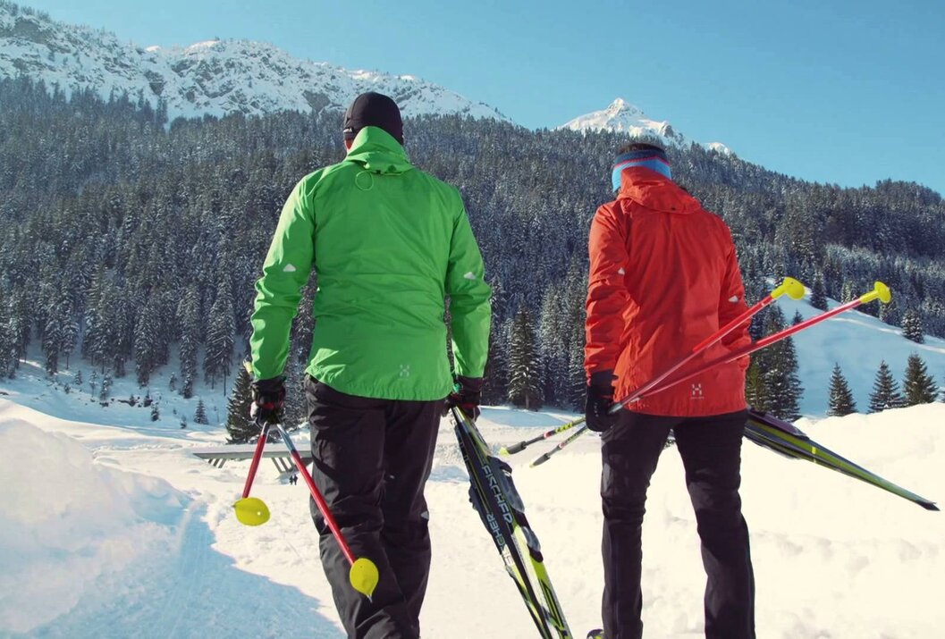 Zwei Langläufer mit Skiern und Stöcken vor verschneiter Berglandschaft