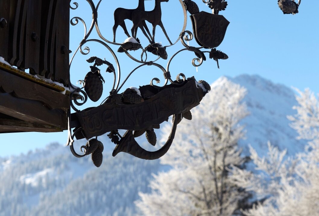 Schwarzes, kunstvolles Schild mit Hirschen und Wappen vor verschneiter Berglandschaft