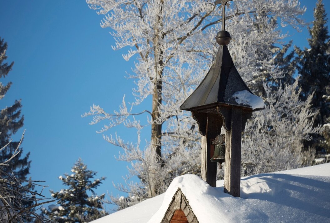 Verschneite Kapelle mit Glockenturm vor blauem Himmel und frostigen Bäumen