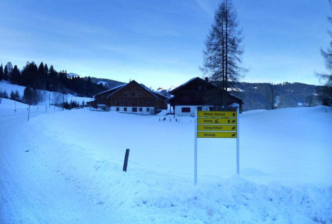 Winterlandschaft mit schneebedeckten Häusern und gelbem Wegweiser unter blauem Himmel