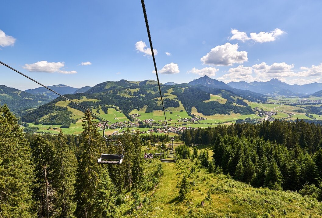 Sessellift über grüne Landschaft mit Bergen und blauem Himmel