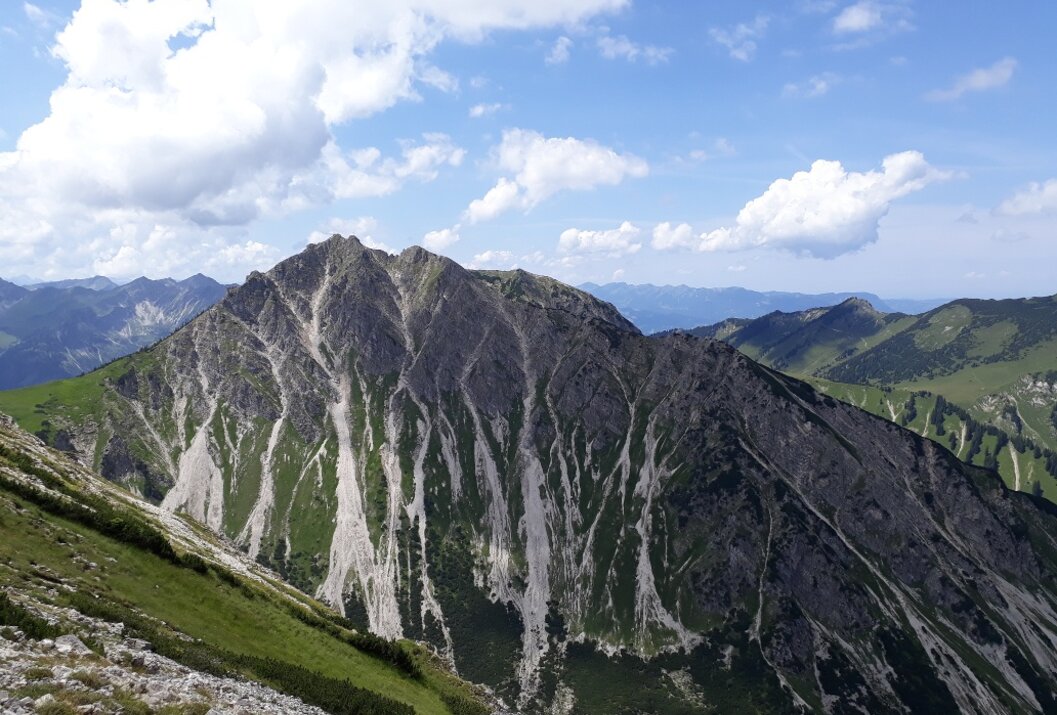 Berglandschaft mit Felsen, grünen Hängen und blauem Himmel mit Wolken