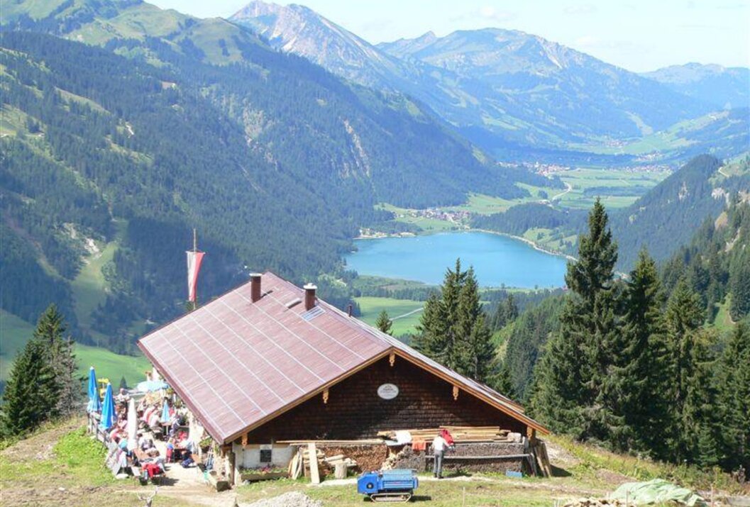 Hütte vor Bergpanorama mit See und bewirteten Gästen