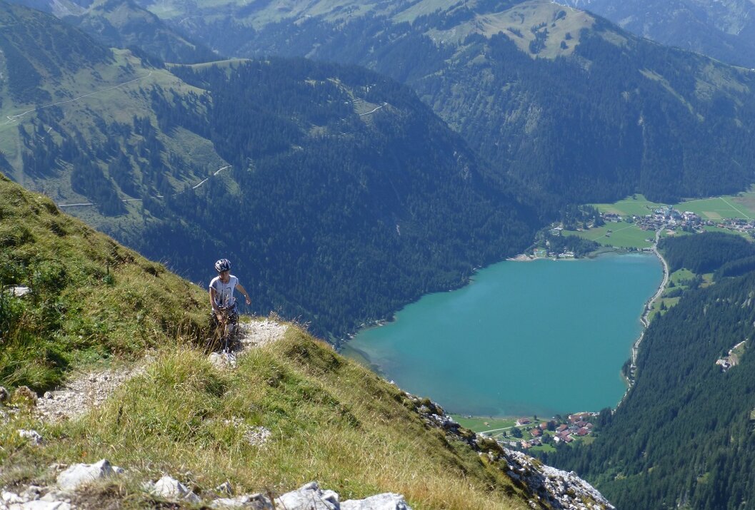 Mountainbiker auf Bergpfad mit Blick auf türkisfarbenen See und grüne Berge