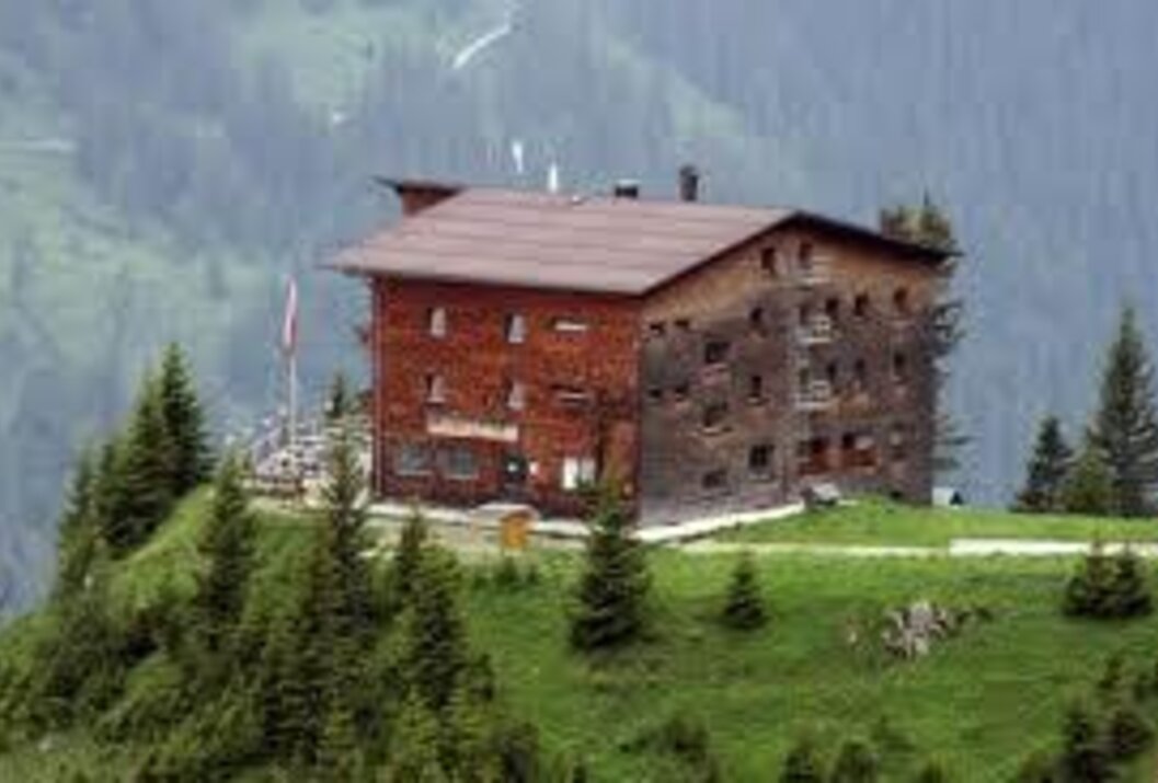 Holzhaus auf grünem Hügel vor Bergkulisse
