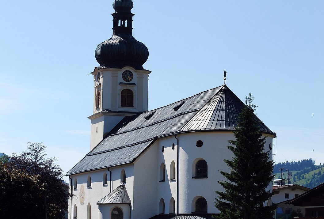Weiße Kirche mit dunklem Turm vor blauem Himmel und grüner Landschaft
