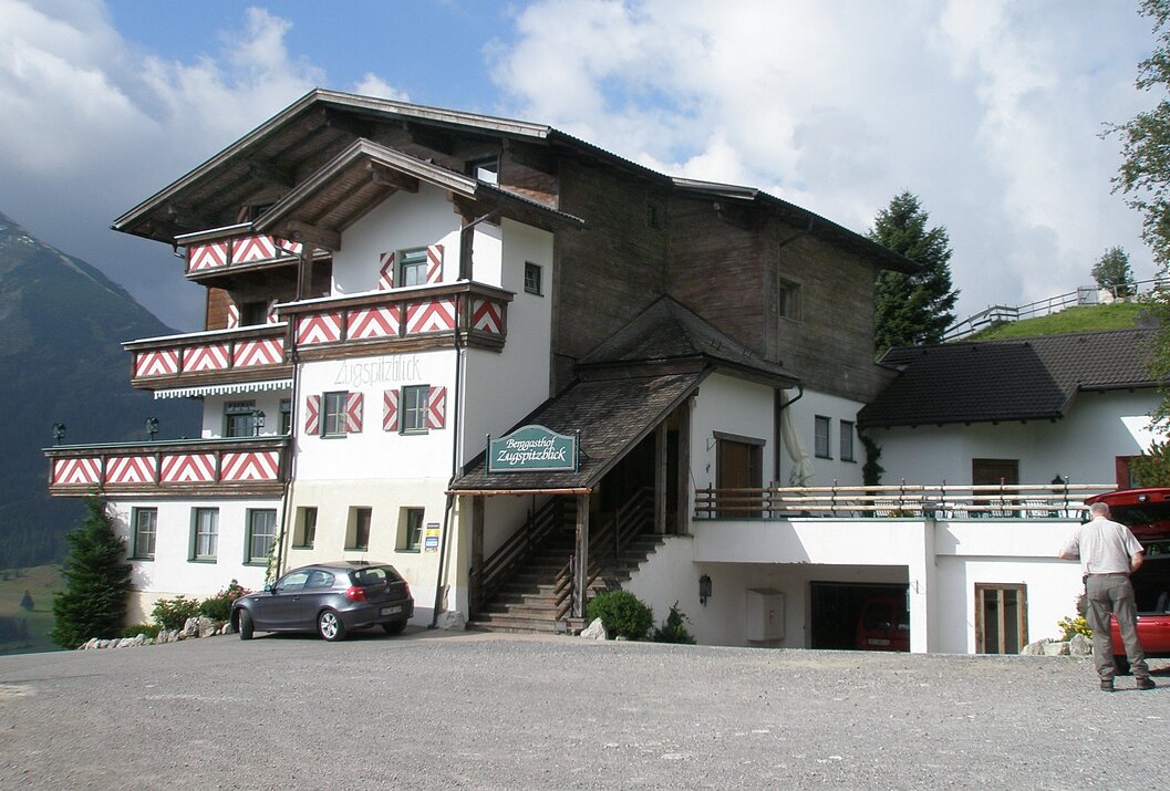 Gasthof in den Bergen mit Auto davor und blauem Himmel