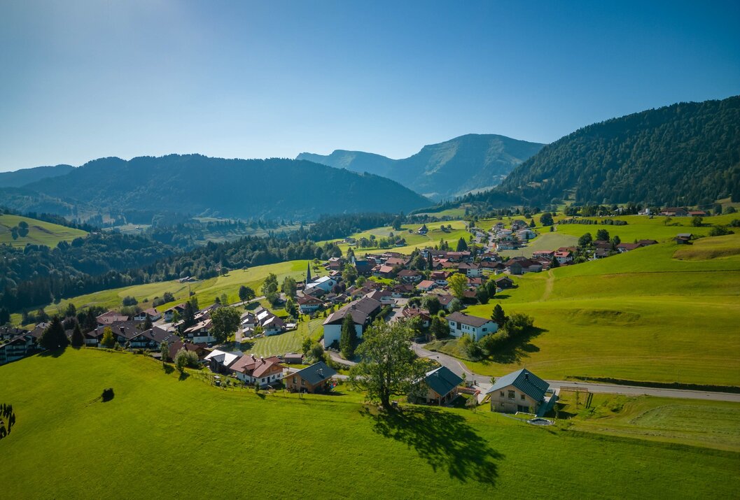 Dorf in grüner Landschaft mit Bergen im Hintergrund unter blauem Himmel