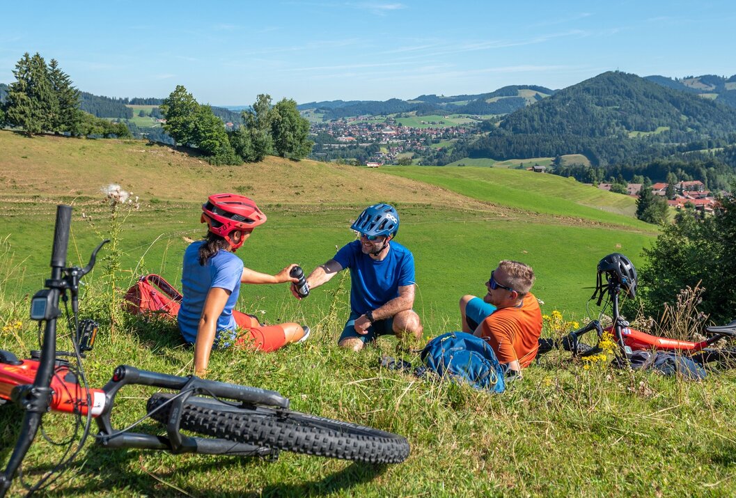 Drei Radfahrer rasten auf einer grünen Wiese mit Blick auf eine Stadt im Tal