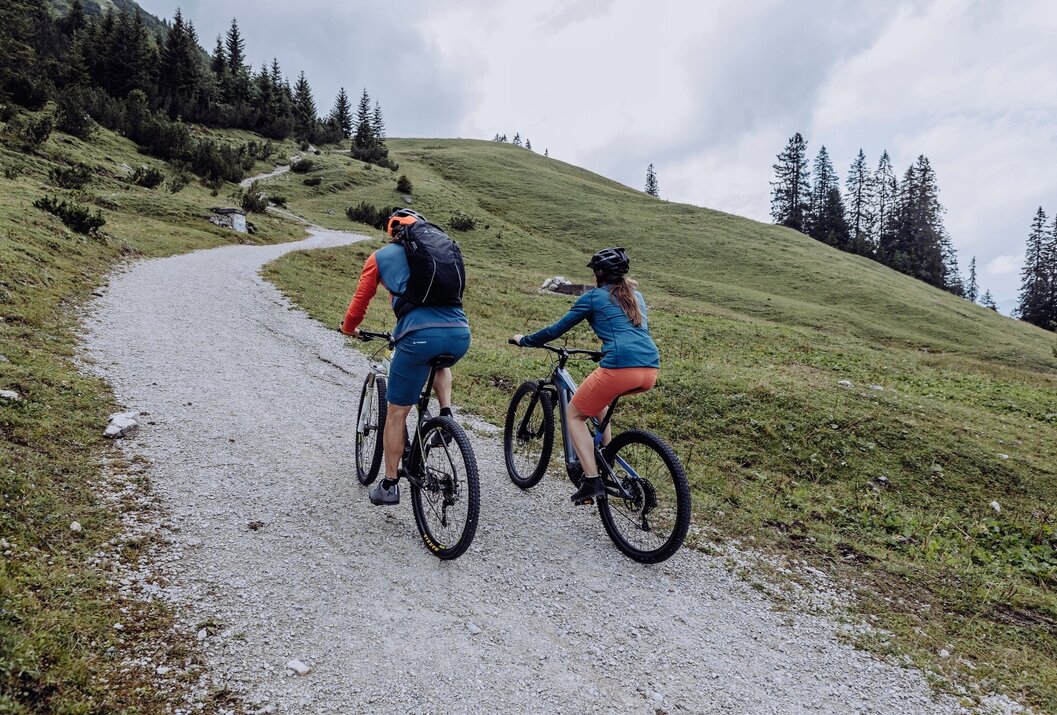 Zwei Personen fahren mit Mountainbikes einen Schotterweg bergauf