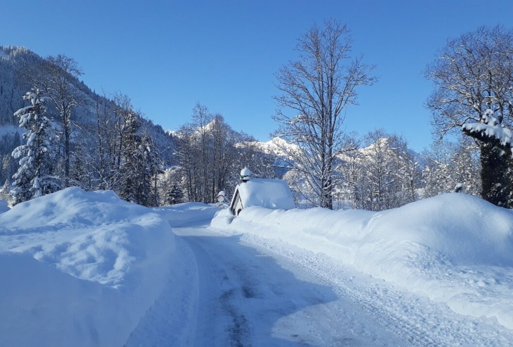 Winterlandschaft mit Schnee bedeckter Straße, Häusern und Bergen unter blauem Himmel