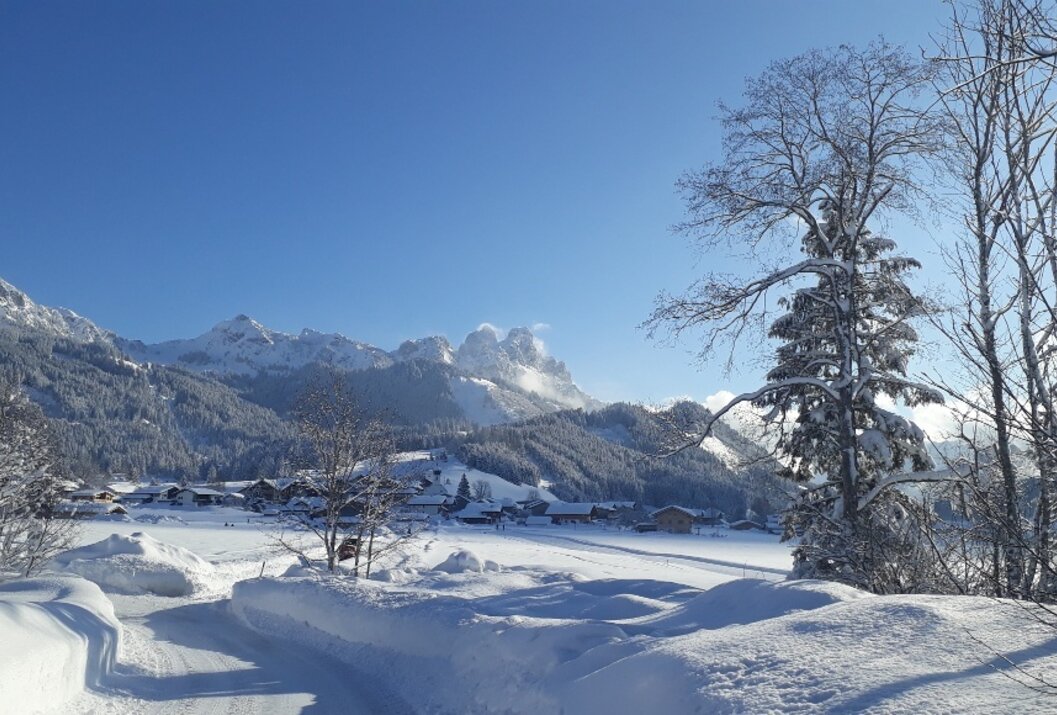 Winterlandschaft mit schneebedeckten Bergen, Bäumen und Häusern unter blauem Himmel