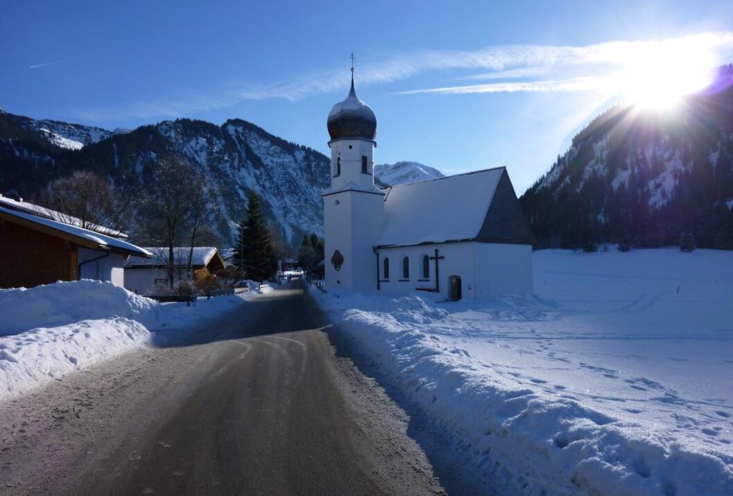Verschneite Kirche vor Bergkulisse unter blauem Himmel