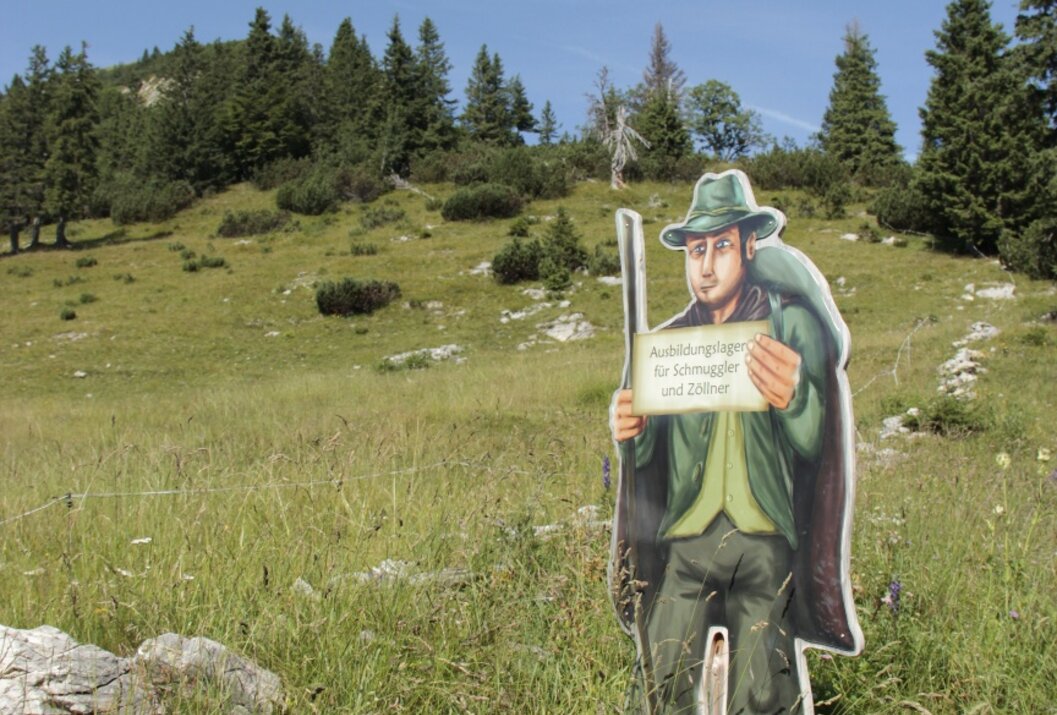 Aufsteller eines Jägers mit Schild auf einer Wiese vor bewaldetem Hügel