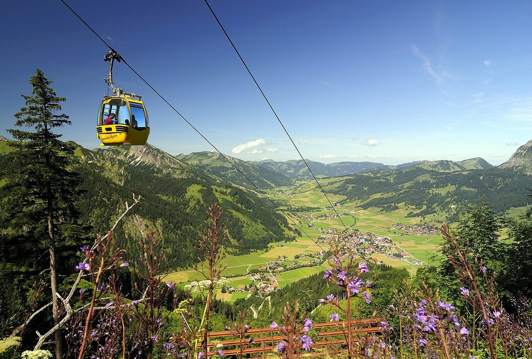 Gelbe Gondelbahn vor Berglandschaft mit Tal und blauem Himmel
