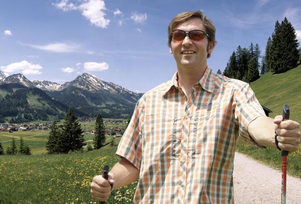 Mann mit Sonnenbrille und Wanderstock vor Berglandschaft
