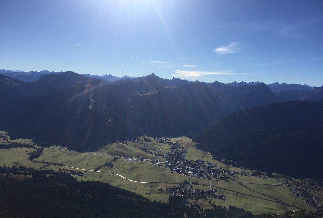 Berglandschaft mit Tal und Häusern unter blauem Himmel mit Sonne