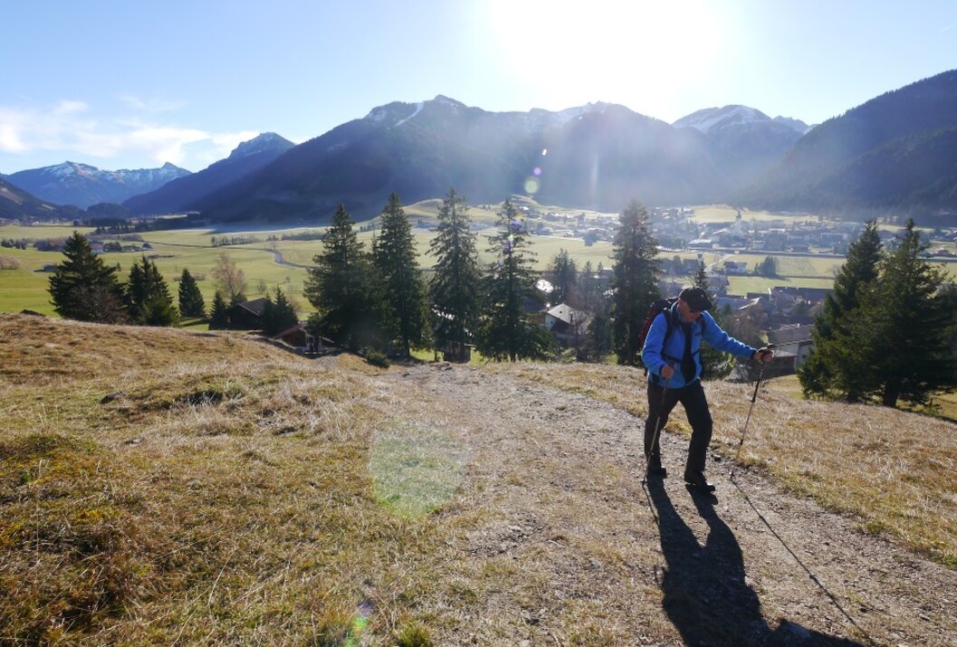 Wanderer mit Stöcken auf Weg, im Hintergrund Tal und Berge