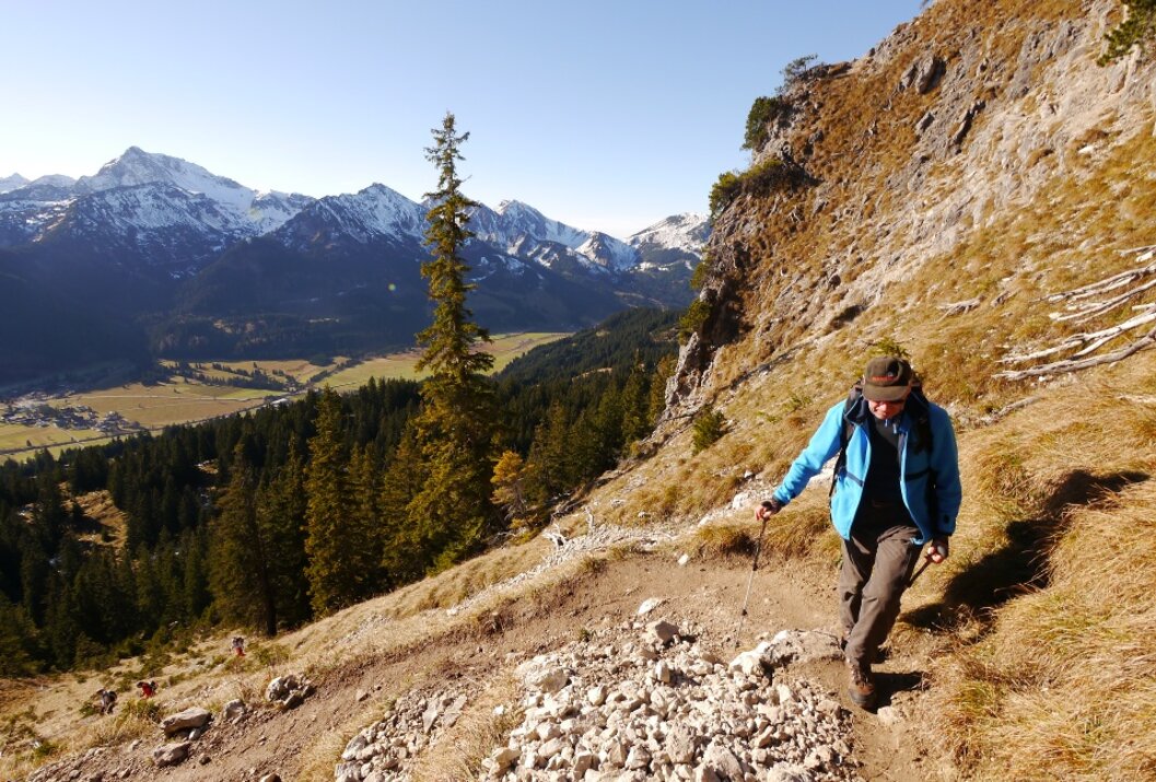 Wanderer mit Rucksack auf Bergpfad, im Hintergrund schneebedeckte Berge und Tal