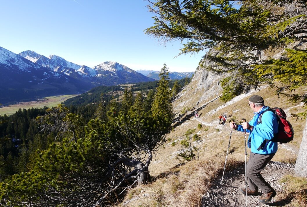 Wanderer auf Bergpfad mit Blick auf schneebedeckte Berge und grüne Täler