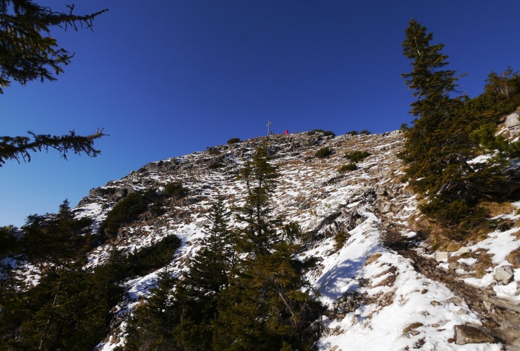 Verschneiter Berggipfel mit Gipfelkreuz unter blauem Himmel