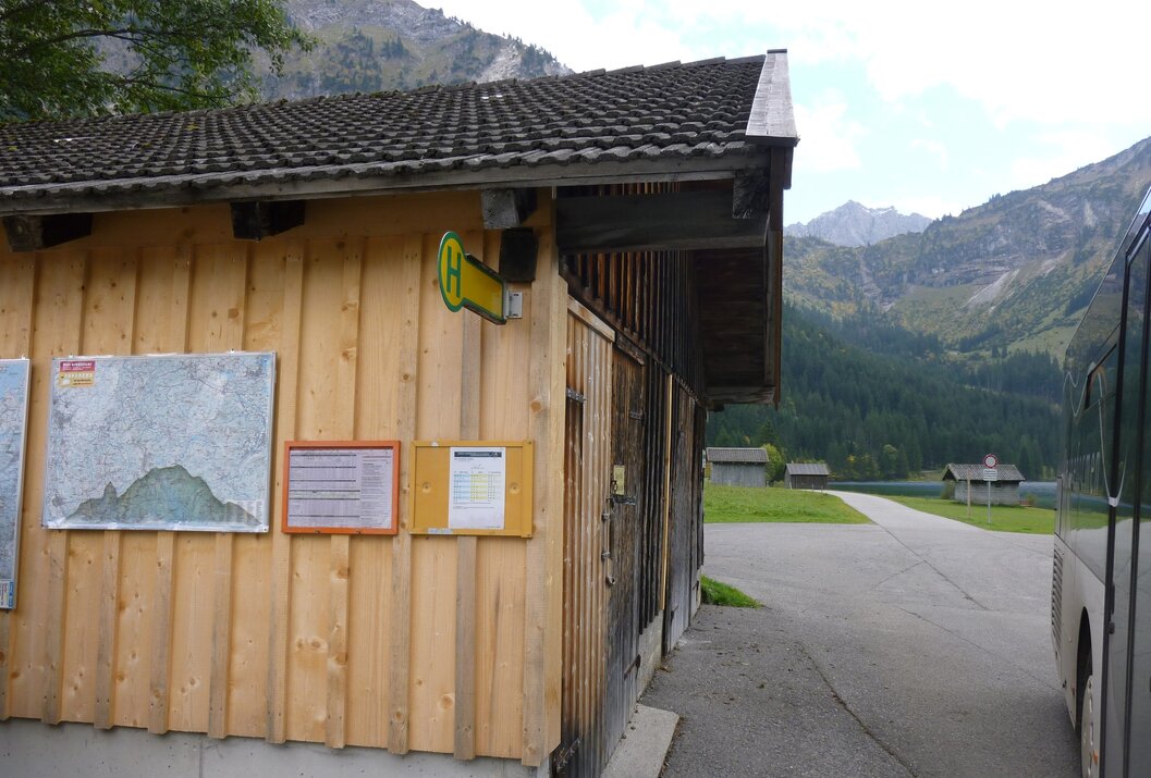 Hölzerne Bushaltestelle mit Aushängen vor Bergkulisse