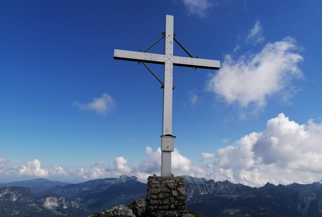 Gipfelkreuz auf Felsen vor Bergpanorama und blauem Himmel mit Wolken