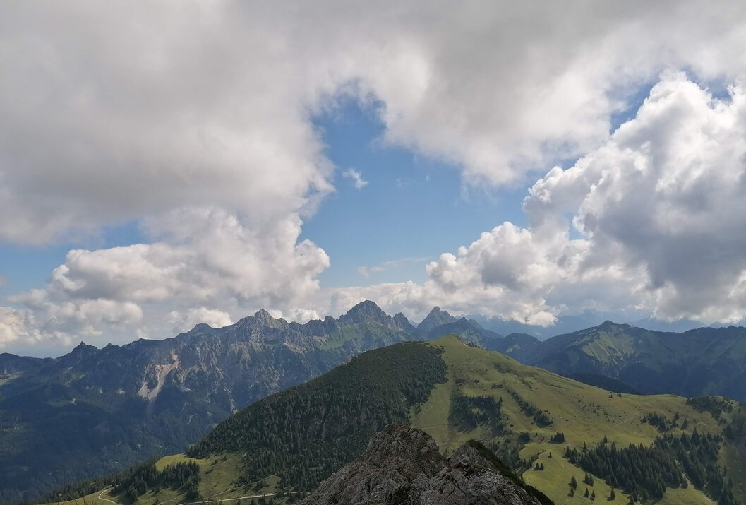 Berglandschaft mit bewaldeten Hügeln unter blauem Himmel mit Wolken