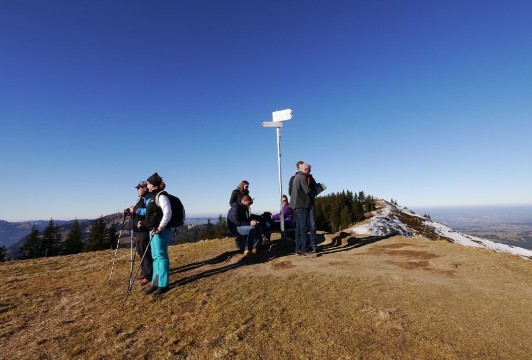 Wandergruppe rastet auf einem Gipfel mit Wegweiser bei strahlendem Sonnenschein