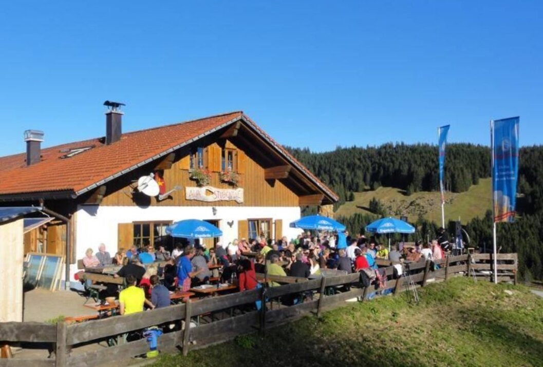 Berghütte mit vielen Menschen auf der Terrasse bei sonnigem Wetter
