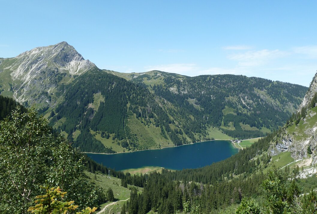 Bergsee umgeben von grünen Bergen und Bäumen unter blauem Himmel