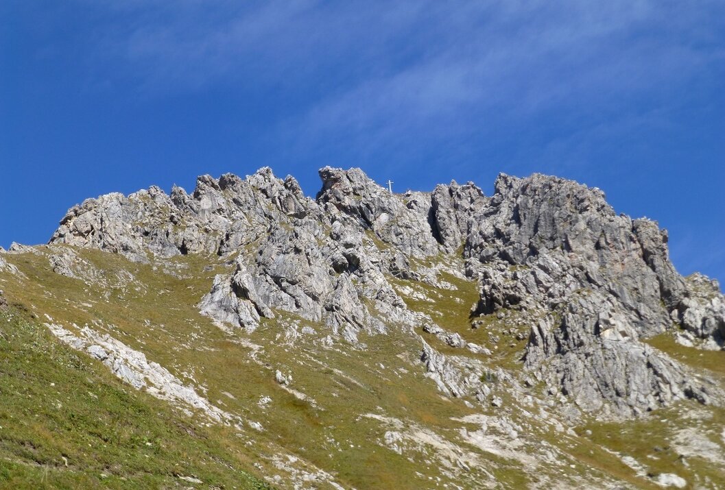 Felsiger Berggipfel unter blauem Himmel mit grüner Vegetation am Hang