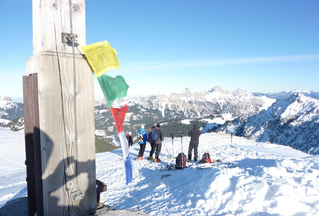 Skifahrer auf schneebedecktem Gipfel mit Gebetsfahnen und Bergpanorama im Hintergrund