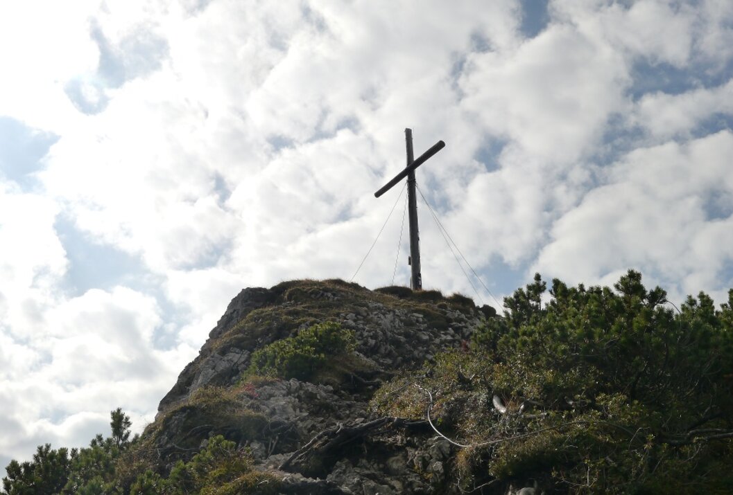 Gipfelkreuz auf felsigem Berg unter bewölktem Himmel