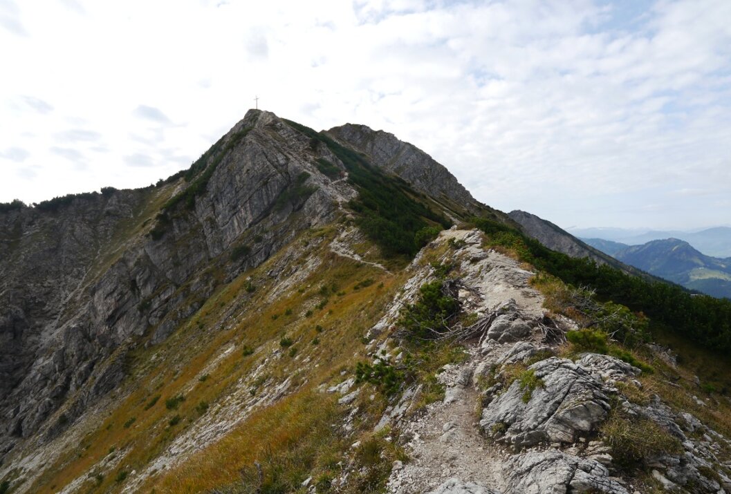 Bergpfad führt zu Gipfel mit Kreuz unter bewölktem Himmel