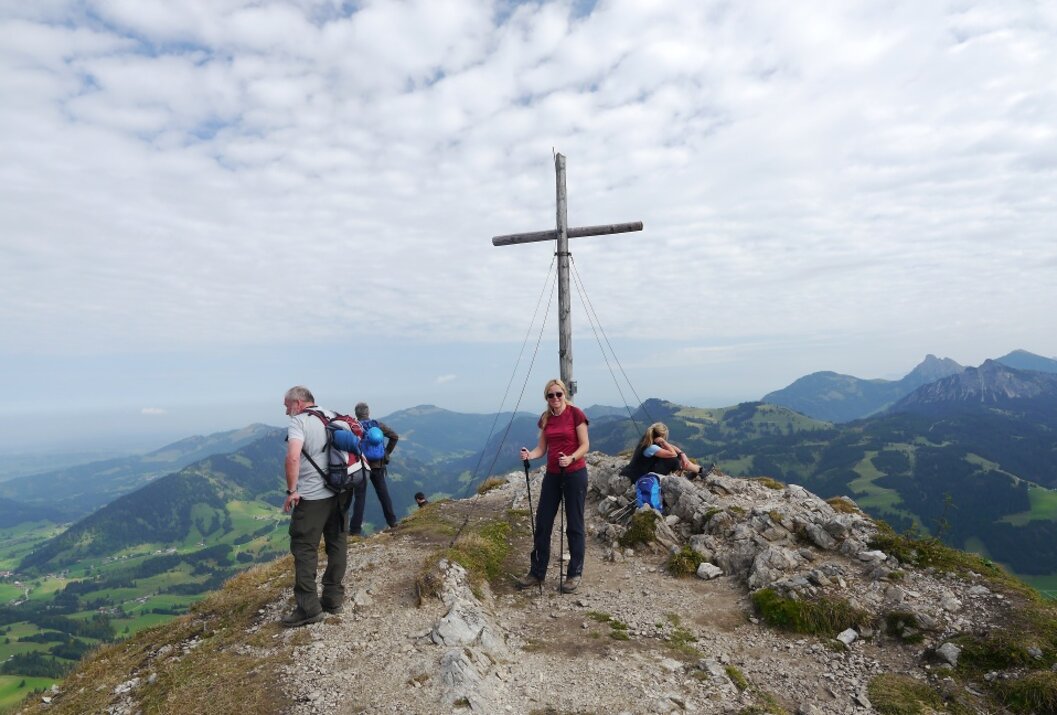 Wanderer stehen am Gipfelkreuz mit Bergpanorama im Hintergrund