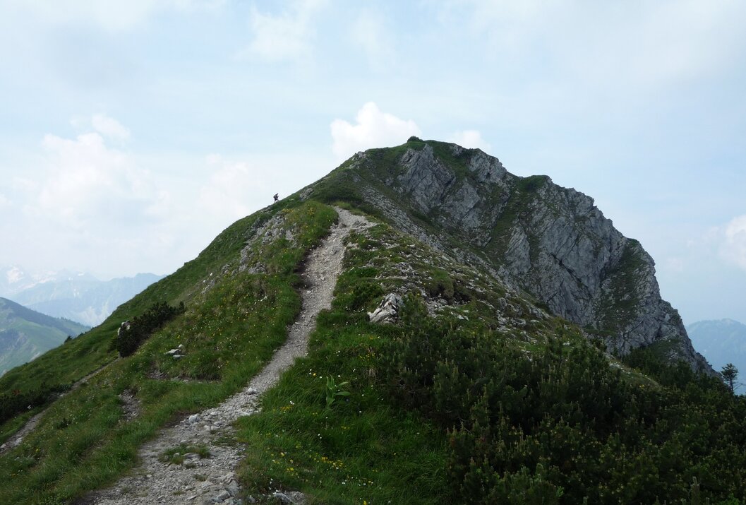 Bergpfad führt zu felsigem Gipfel unter blauem Himmel