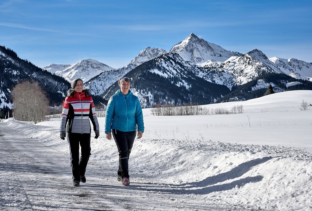 Zwei Frauen wandern im Winter vor schneebedeckten Bergen