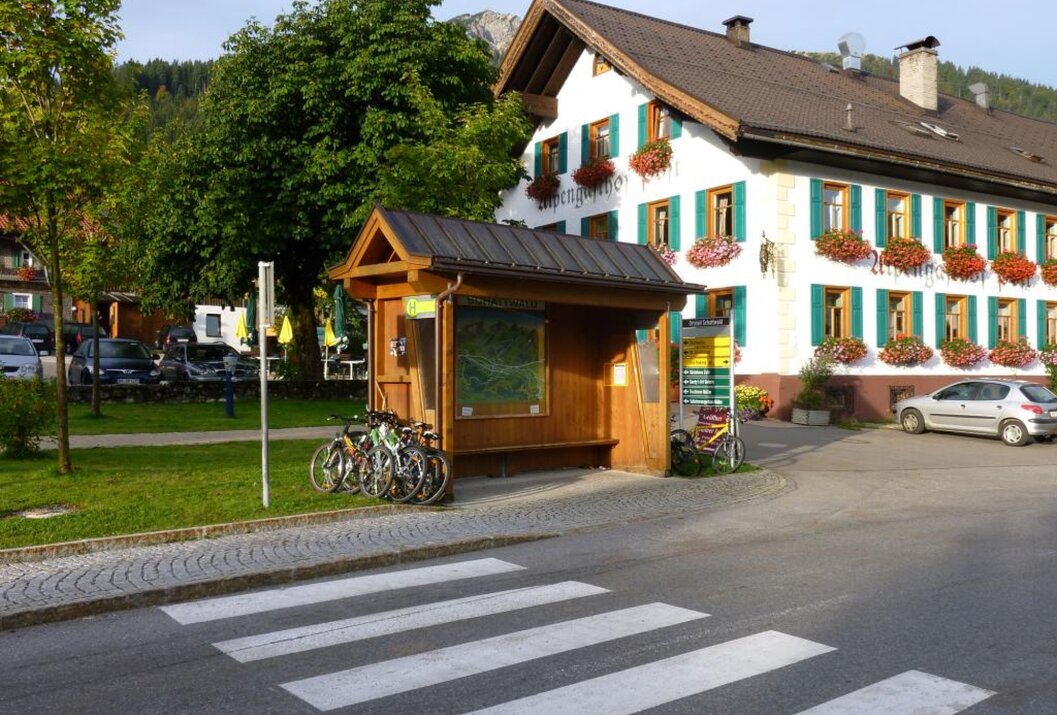 Bushaltestelle mit Fahrrädern vor einem Haus mit Blumenkästen und einem Baum