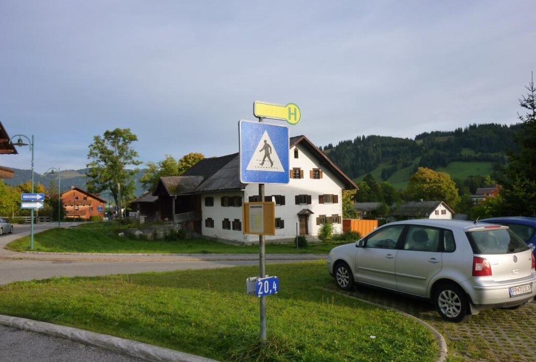 Fußgängerweg-Schild vor weißem Haus und geparktem Auto auf Rasenfläche
