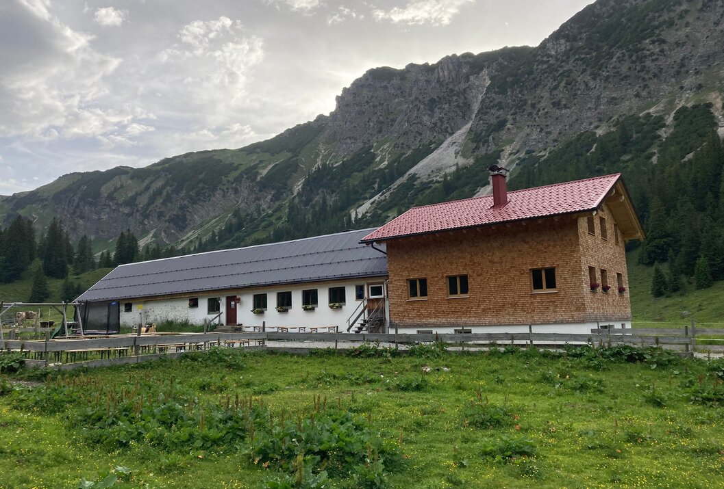 Hütte mit rotem Dach vor Berglandschaft und grüner Wiese