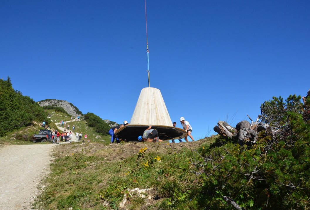 Menschen tragen kegelförmige Konstruktion auf Bergwiese