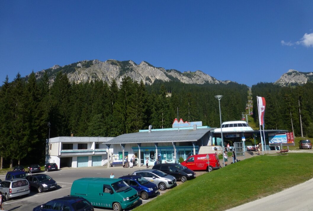Gebäude mit Parkplatz vor bewaldetem Berg unter blauem Himmel